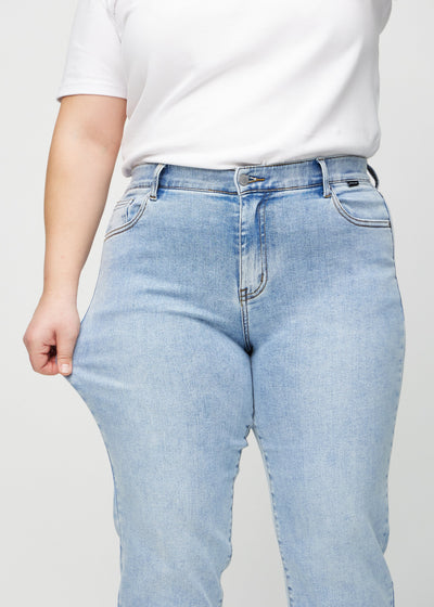 Plus-size model strækker jeansene ved låret for at vise stretch.